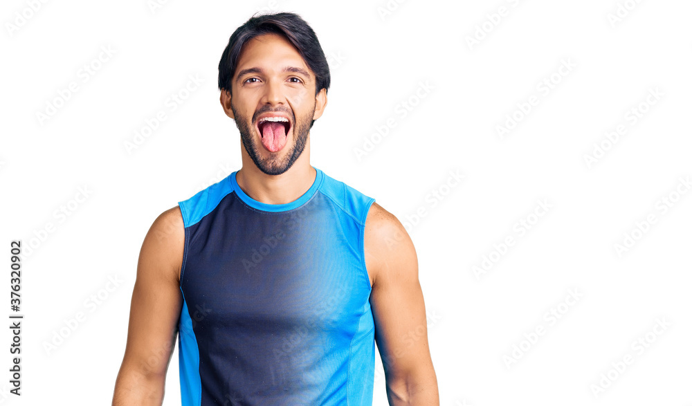 Handsome hispanic man wearing sportswear sticking tongue out happy with funny expression. emotion concept.