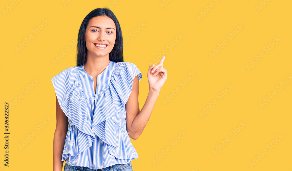 Young beautiful latin girl wearing casual clothes with a big smile on face, pointing with hand finger to the side looking at the camera. Young beautiful latin girl wearing casual clothes with a big smile on face, pointing with hand finger to the side looking at the camera.