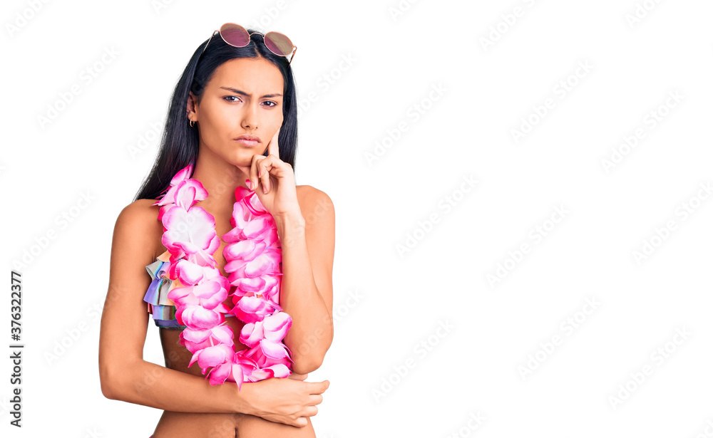 Young beautiful latin girl wearing bikini and hawaiian lei serious face thinking about question with hand on chin, thoughtful about confusing idea Young beautiful latin girl wearing bikini and hawaiian lei serious face thinking about question with hand on chin, thoughtful about confusing idea