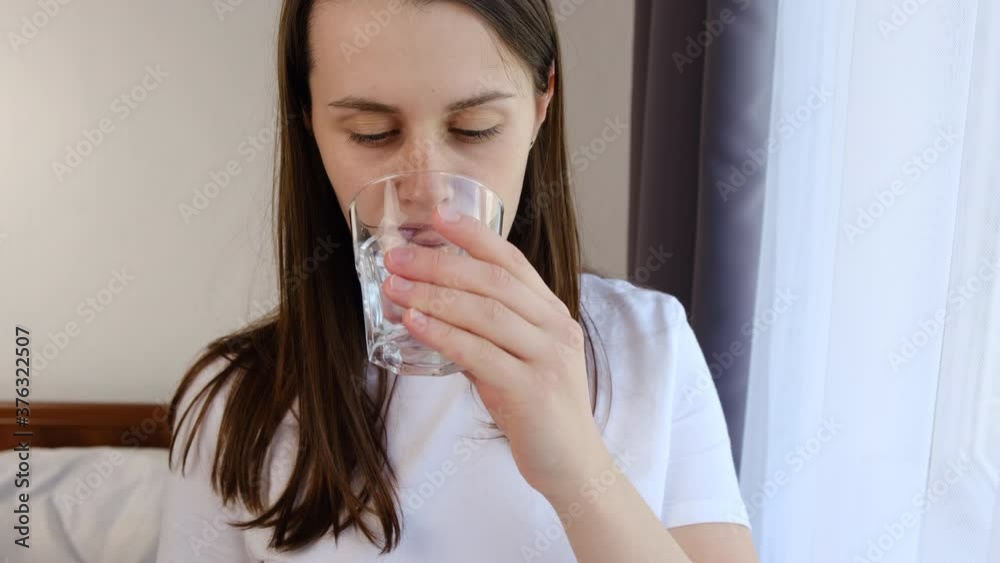 Young attractive woman standing near window hold glass refreshing drinking pure mineral water in morning, close up of cute female enjoying aqua having good habits. Healthy lifestyle concept Young attractive woman standing near window hold glass refreshing drinking pure mineral water in morning, close up of cute female enjoying aqua having good habits. Healthy lifestyle concept
