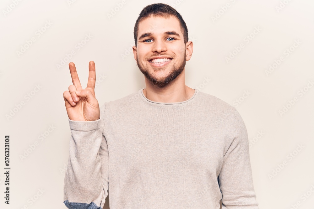 Young handsome man wearing casual sweater smiling with happy face winking at the camera doing victory sign. number two. Young handsome man wearing casual sweater smiling with happy face winking at the camera doing victory sign. number two.