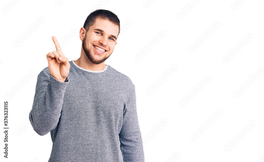Young handsome man wearing casual sweater showing and pointing up with finger number one while smiling confident and happy. Young handsome man wearing casual sweater showing and pointing up with finger number one while smiling confident and happy.