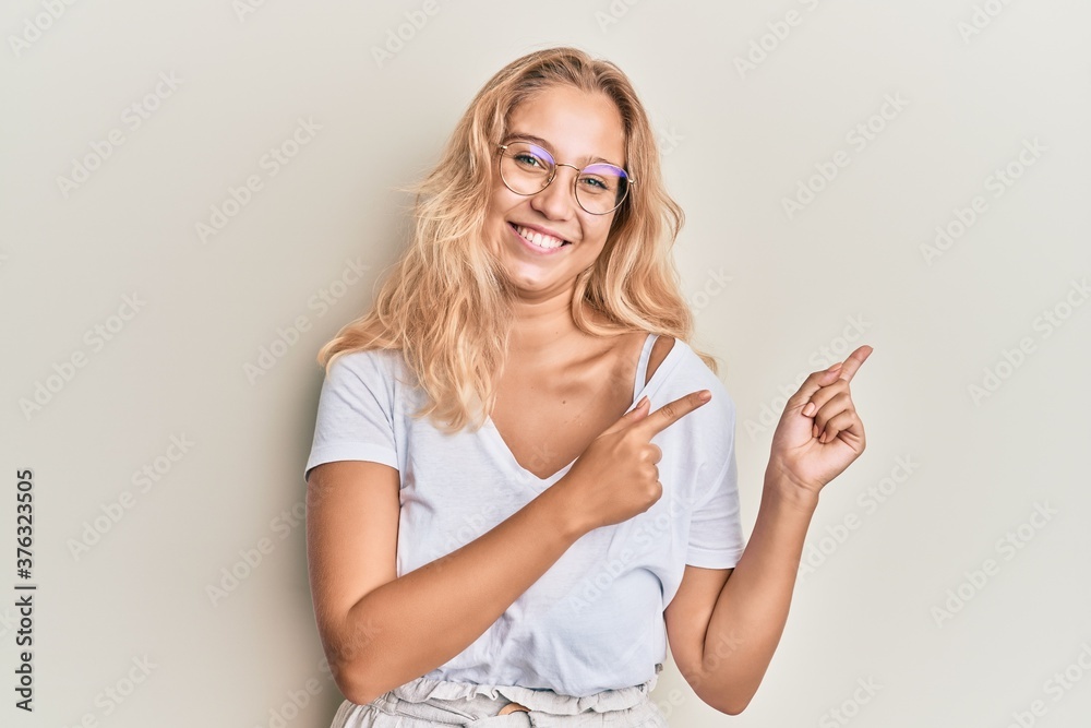Young blonde girl wearing casual clothes and glasses smiling and looking at the camera pointing with two hands and fingers to the side. Young blonde girl wearing casual clothes and glasses smiling and looking at the camera pointing with two hands and fingers to the side.
