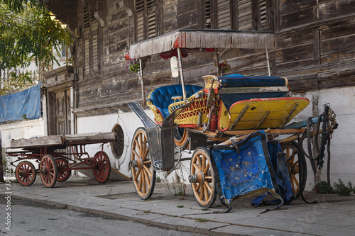 an old and abandoned horse carriage and cart load stay in front of old wooden house.