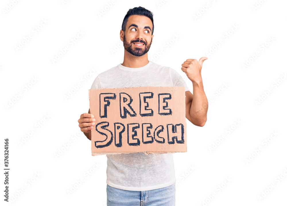 Young hispanic man holding free speech banner pointing thumb up to the side smiling happy with open mouth