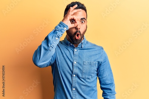 Young hispanic man wearing casual clothes doing ok gesture shocked with surprised face, eye looking through fingers. unbelieving expression.