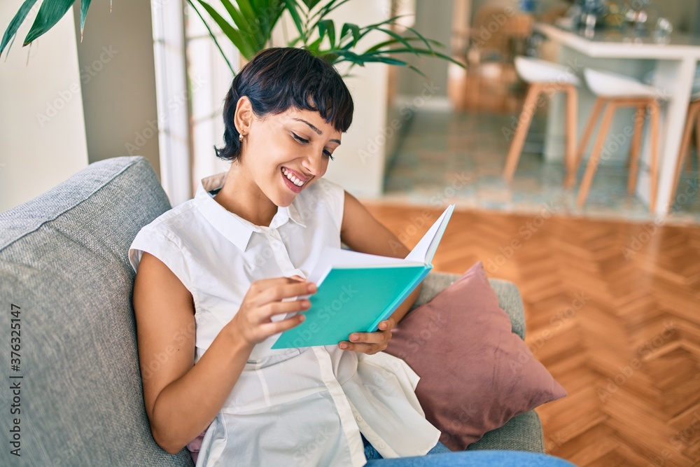 Beautiful brunette woman with short hair at home reading a book sitting on the sofa Beautiful brunette woman with short hair at home reading a book sitting on the sofa
