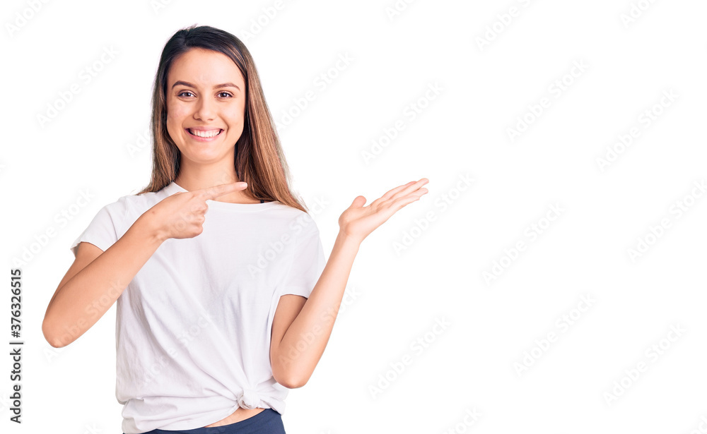 Young beautiful girl wearing casual t shirt amazed and smiling to the camera while presenting with hand and pointing with finger. Young beautiful girl wearing casual t shirt amazed and smiling to the camera while presenting with hand and pointing with finger.