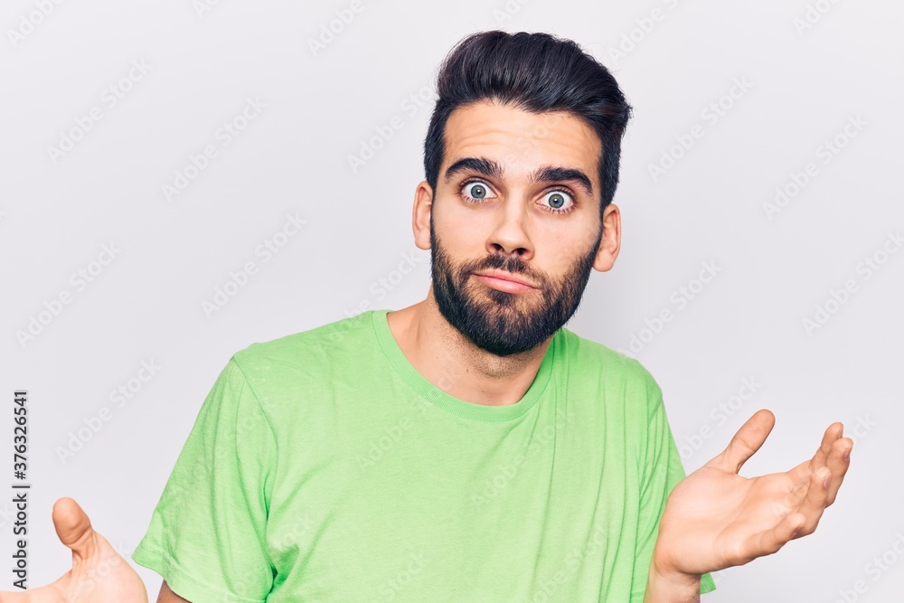 Young handsome man with beard wearing casual t-shirt clueless and confused expression with arms and hands raised. doubt concept. Young handsome man with beard wearing casual t-shirt clueless and confused expression with arms and hands raised. doubt concept.