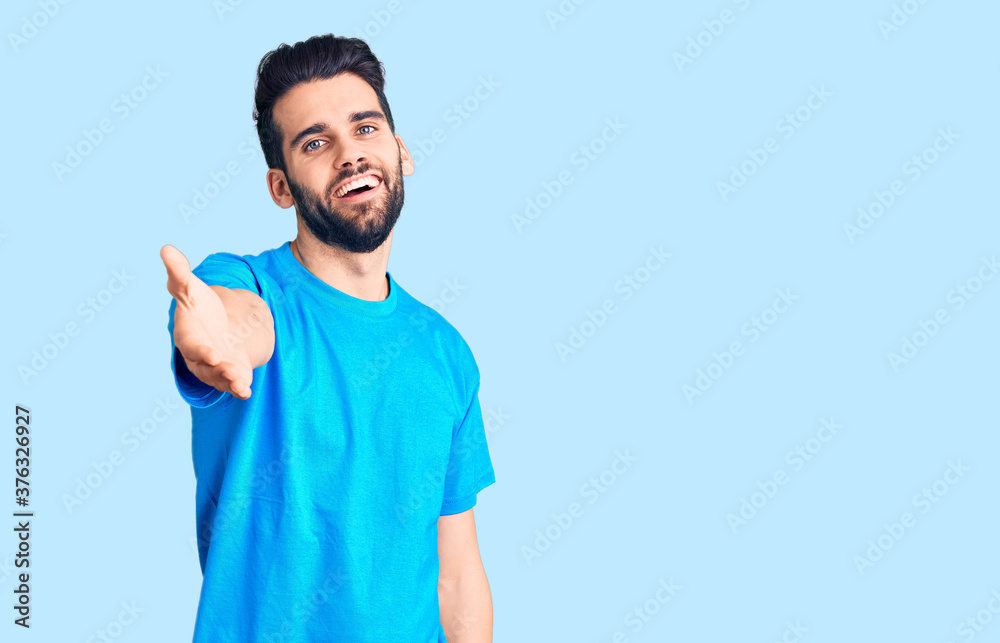 Young handsome man with beard wearing casual t-shirt smiling cheerful offering palm hand giving assistance and acceptance. Young handsome man with beard wearing casual t-shirt smiling cheerful offering palm hand giving assistance and acceptance.