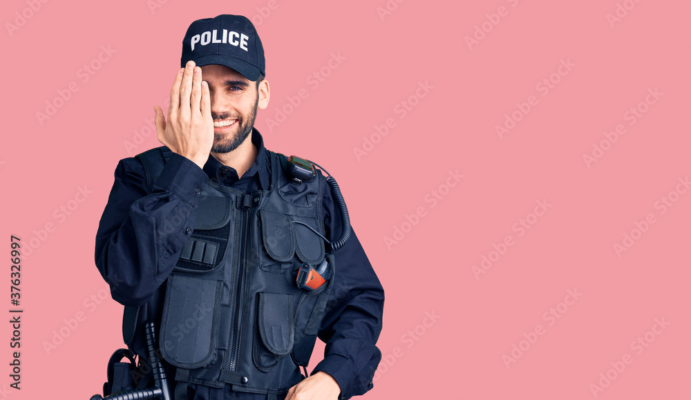 Young handsome man with beard wearing police uniform covering one eye with hand, confident smile on face and surprise emotion. Young handsome man with beard wearing police uniform covering one eye with hand, confident smile on face and surprise emotion.
