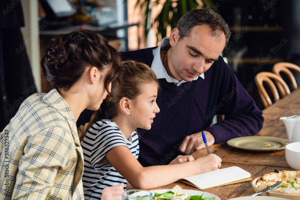 Family, parenthood, communication and people concept - happy mother, father and little girl having dinner and talking at restaurant or cafe. Family, parenthood, communication and people concept - happy mother, father and little girl having dinner and talking at restaurant or cafe.