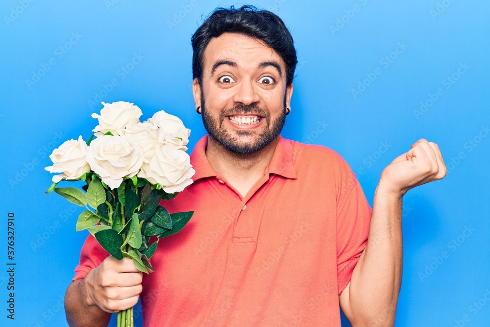 Young hispanic man holding flowers screaming proud, celebrating victory and success very excited with raised arm Young hispanic man holding flowers screaming proud, celebrating victory and success very excited with raised arm
