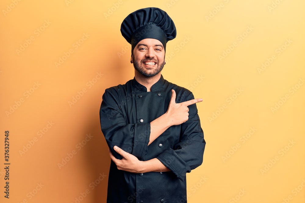 Young hispanic man wearing cooker uniform smiling cheerful pointing with hand and finger up to the side Young hispanic man wearing cooker uniform smiling cheerful pointing with hand and finger up to the side