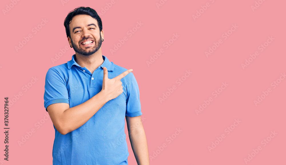 Fototapeta premium Young hispanic man wearing casual clothes cheerful with a smile of face pointing with hand and finger up to the side with happy and natural expression on face