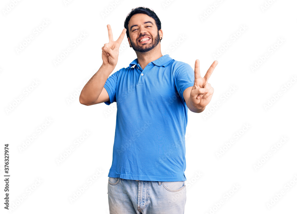 Young hispanic man wearing casual clothes smiling looking to the camera showing fingers doing victory sign. number two. Young hispanic man wearing casual clothes smiling looking to the camera showing fingers doing victory sign. number two.