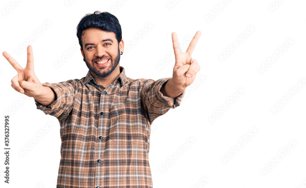 Young hispanic man wearing casual clothes smiling with tongue out showing fingers of both hands doing victory sign. number two. Young hispanic man wearing casual clothes smiling with tongue out showing fingers of both hands doing victory sign. number two.
