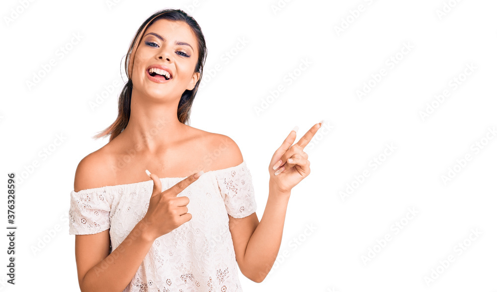 Plakat Młoda piękna kobieta nosi ubranie, uśmiechając się i patrząc na kamerę, wskazując dwiema rękami i palcami na bok.