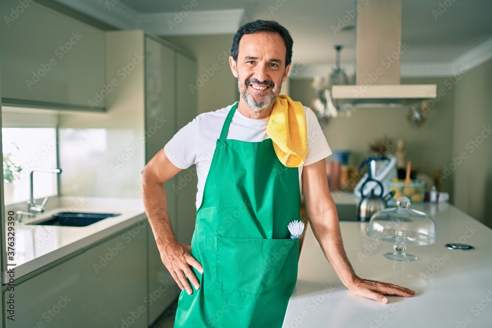 Middle age housekeeping man with beard smiling happy standing at the kitchen Middle age housekeeping man with beard smiling happy standing at the kitchen