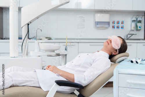 A young woman, a dentist or an intern, rests on the chair in the dentist's office in a very relaxed pose.