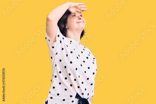 Brunette woman with down syndrome wearing casual clothes very happy and smiling looking far away with hand over head. searching concept.