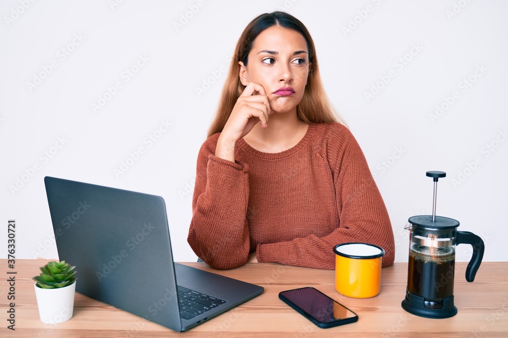 Young brunette woman working at the office drinking a cup of coffee thinking concentrated about doubt with finger on chin and looking up wondering Young brunette woman working at the office drinking a cup of coffee thinking concentrated about doubt with finger on chin and looking up wondering