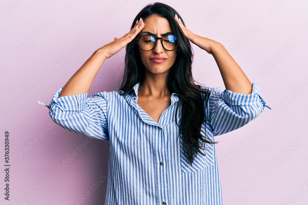 Beautiful hispanic woman wearing casual clothes and glasses with hand on head, headache because stress. suffering migraine. Beautiful hispanic woman wearing casual clothes and glasses with hand on head, headache because stress. suffering migraine.