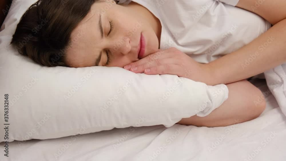 Close up of young woman having problems with her sleep, moving on bed, unable to fall asleep, feels headache because of insomnia or discomfort, lying on uncomfortable mattress. Depression concept Close up of young woman having problems with her sleep, moving on bed, unable to fall asleep, feels headache because of insomnia or discomfort, lying on uncomfortable mattress. Depression concept