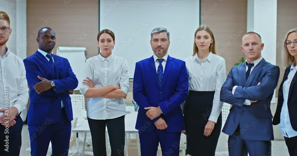 Team of motivated businessmen in business suits. Young men and women stand in a row and look seriously, portrait view. Zoom in the camera. 4k, ProRes Team of motivated businessmen in business suits. Young men and women stand in a row and look seriously, portrait view. Zoom in the camera. 4k, ProRes