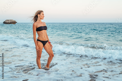Young woman in black bikini on the beach in the evening