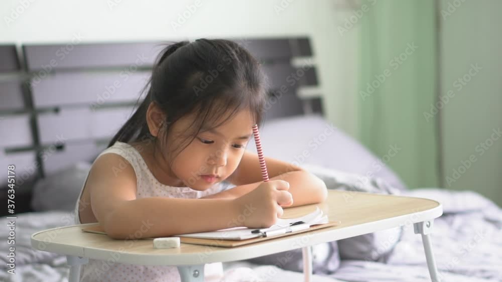 asian child student or kid girl writing drawing and enjoy doing homework or happy read learn and training write on paper with table by stay home safe and back to school study online in bedroom on slow