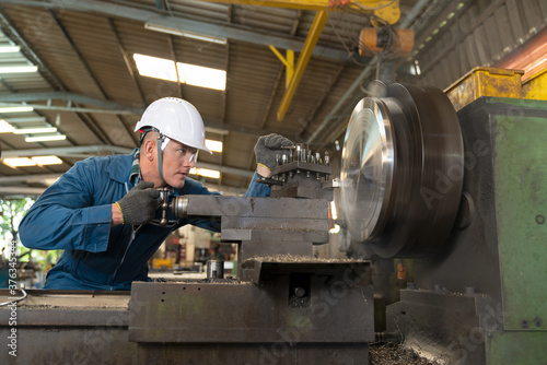 Male worker working on a lathe machine in metal industry factory on a business day. Professional engineer wearing a hard hat and safety glasses operating CNC milling machine in manufacturing workshop