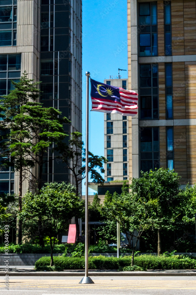 Malaysian flag on pole, waving under the wind by sunny day with blue sky in city environment