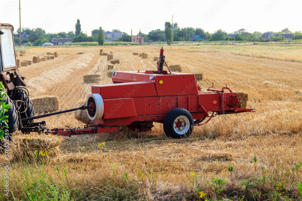 Fototapeta premium Rectangular baler discharges a straw bale in a field during the harvesting process