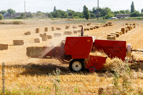 Rectangular baler discharges a straw bale in a field during the harvesting process photo