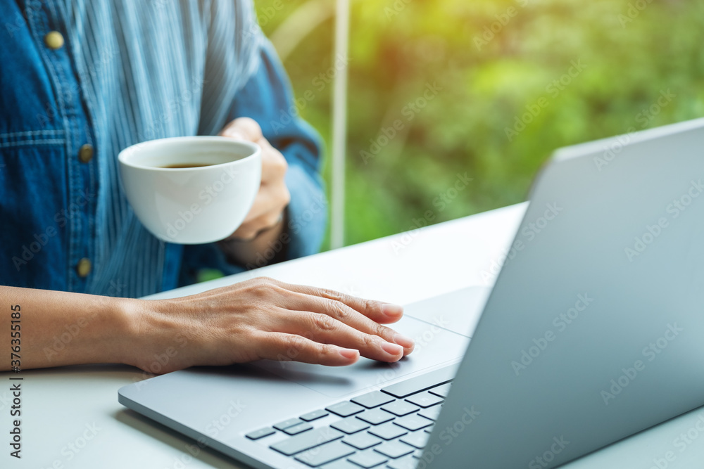 Closeup image of a woman working and touching on laptop computer touchpad while drinking coffee Closeup image of a woman working and touching on laptop computer touchpad while drinking coffee