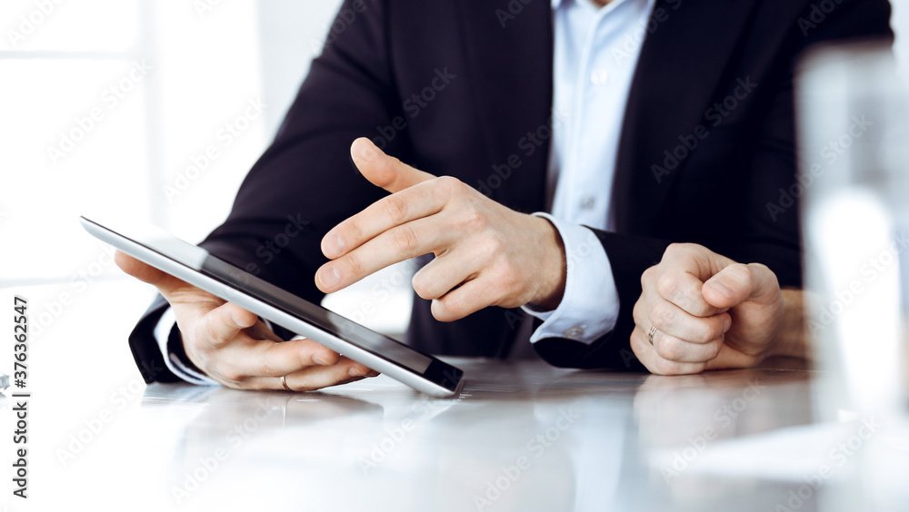 Business people using tablet computer while working together at the desk in modern office. Unknown businessman or male entrepreneur with colleague at workplace. Teamwork and partnership concept Business people using tablet computer while working together at the desk in modern office. Unknown businessman or male entrepreneur with colleague at workplace. Teamwork and partnership concept