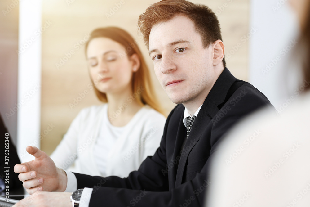 Businessman headshot at meeting in sunny office. Unknown entrepreneur sitting with colleagues at the background Businessman headshot at meeting in sunny office. Unknown entrepreneur sitting with colleagues at the background