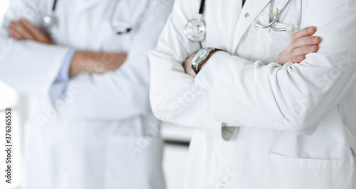 Group of unknown doctors standing as a team with arms crossed in hospital office, close-up. Medical help, insurance in health care and medicine concept