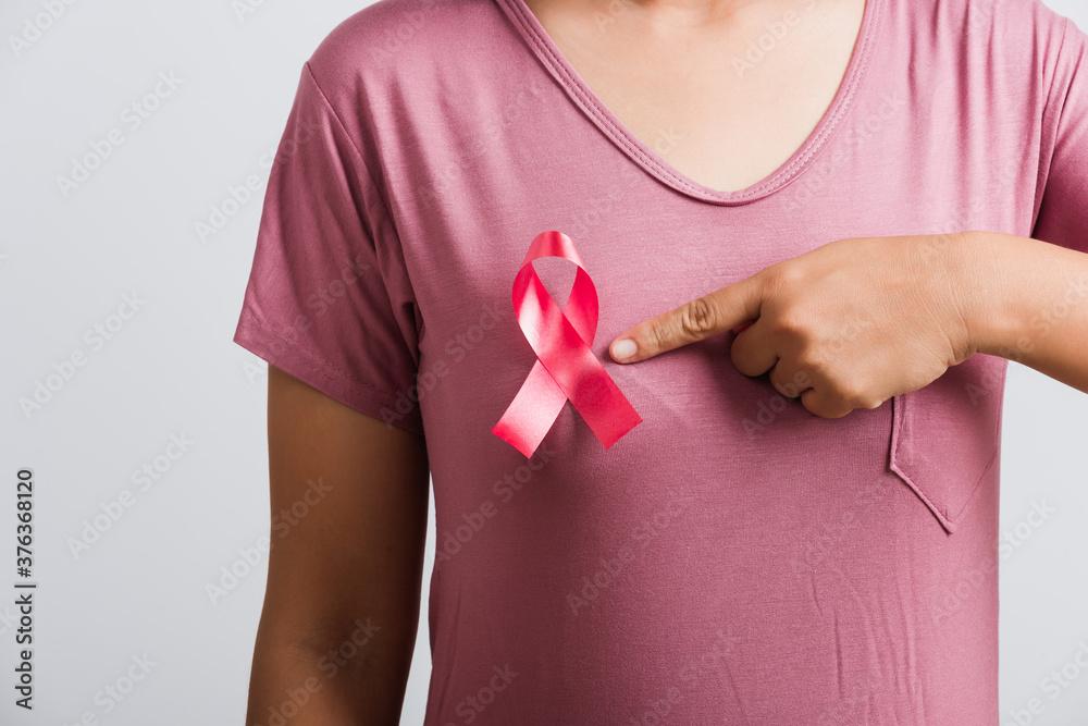 Breast cancer awareness healthcare and medicine concept. Close up Asian woman wear pink shirt pointing finger to pink breast cancer awareness ribbon, studio shot isolated on white background Breast cancer awareness healthcare and medicine concept. Close up Asian woman wear pink shirt pointing finger to pink breast cancer awareness ribbon, studio shot isolated on white background