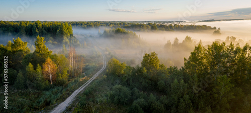 Early morning landscape. Foggy forest. Footpath trough the forest in a thick mysterious fog at sunrise. View from above