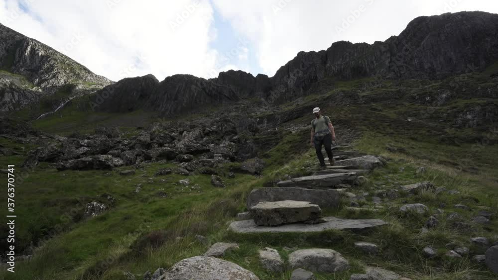 Hiking man walking down stone steps in the mountains of Snowdonia in Wales UK Hiking man walking down stone steps in the mountains of Snowdonia in Wales UK