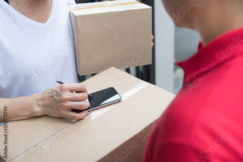 Asian delivery man in red uniform delivering parcel box to woman recipient at home
