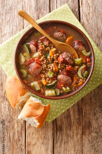 Sausage lentil soup with tomatoes, zucchini, carrots, celery and onions close-up in a plate on the table. vertical top view from above