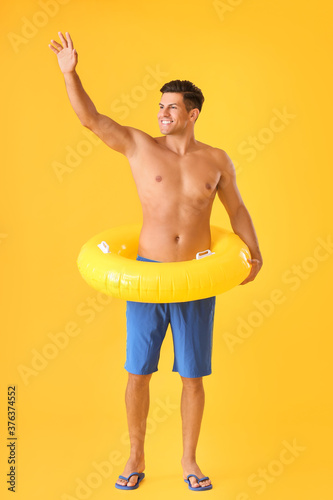 Happy young man with inflatable ring on color background