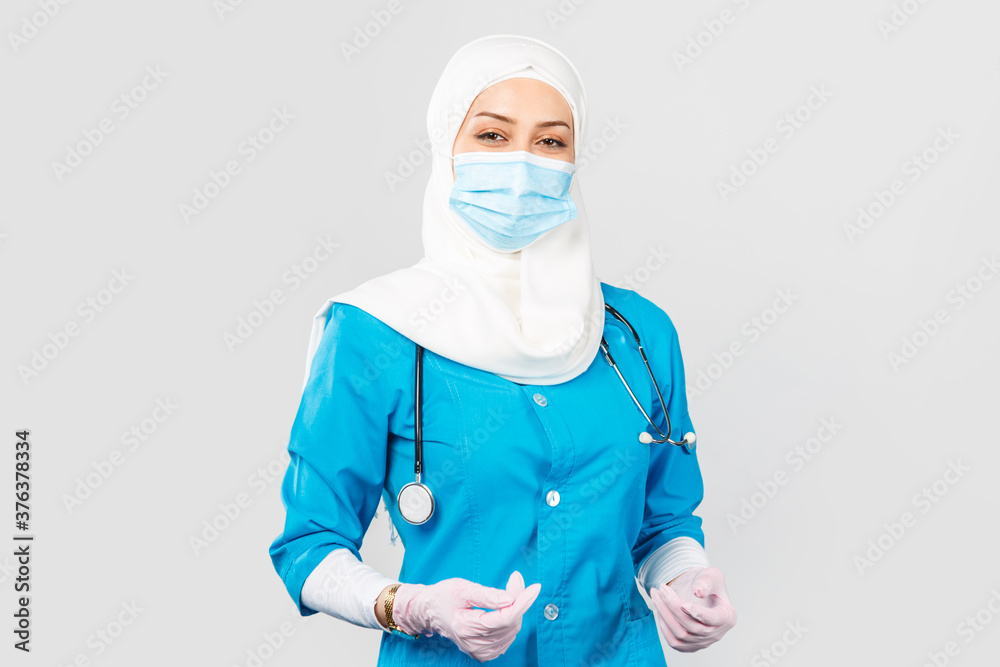 friendly Muslim doctor or nurse wearing hijab and medical face mask and gloves on a gray background. friendly Muslim doctor or nurse wearing hijab and medical face mask and gloves on a gray background.
