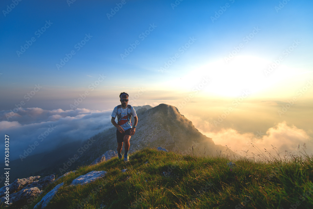Mountain runner training at sunset with clouds below