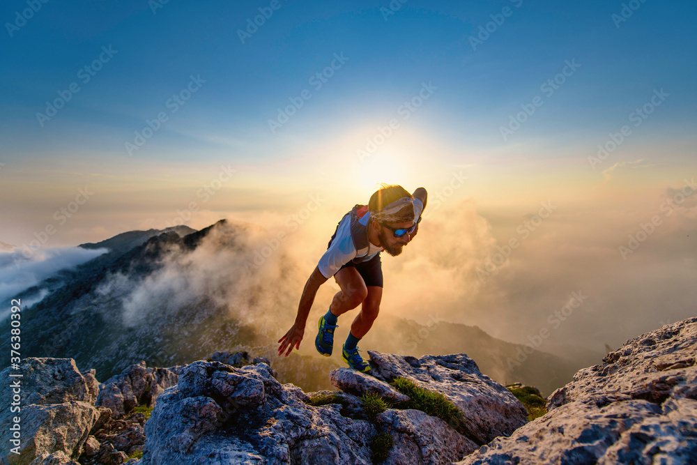 Fotografie Sky runner man uphill on rocks at sunset
