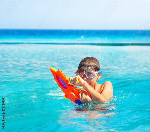 Portrait of a boy with water gun squirt toy in the pool near sea wearing swimming mask