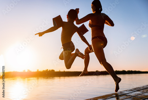 Single mother with her son enjoying on vacation jumping in lake from pier on summer day.